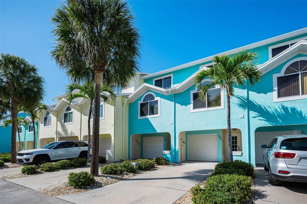 A row of colorful townhomes with attached garages and palm trees under a clear sky — 140 MARCDALE BOULEVARD, INDIAN ROCKS BEACH, FL