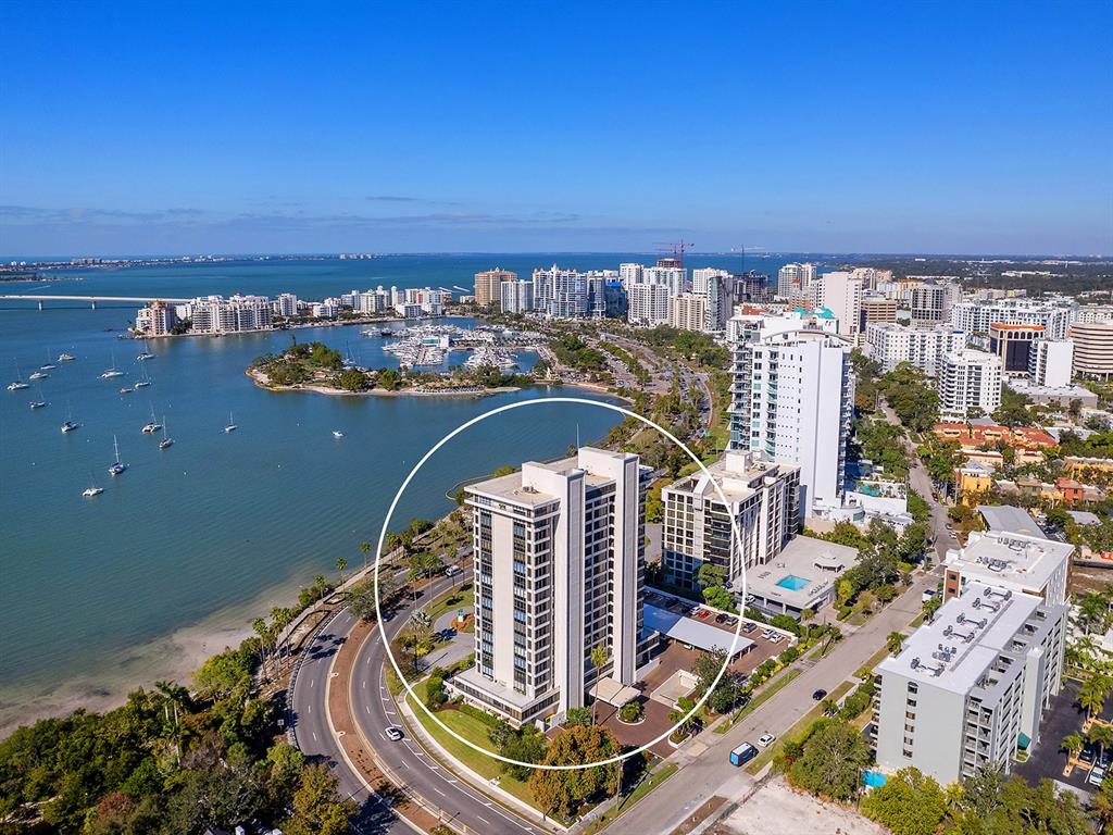 An aerial view shows a tall residential building circled near a waterfront with docked boats — 770 S PALM AVENUE UNIT 1201, SARASOTA, FL