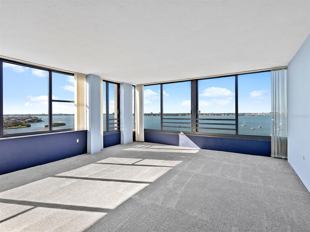 An empty living room with gray carpet, light blue walls, and large windows overlooking water — 770 S PALM AVENUE UNIT 1201, SARASOTA, FL