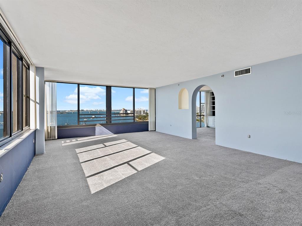An empty room with gray carpet, an arched doorway, and floor-to-ceiling windows overlooking a bay — 770 S PALM AVENUE UNIT 1201, SARASOTA, FL