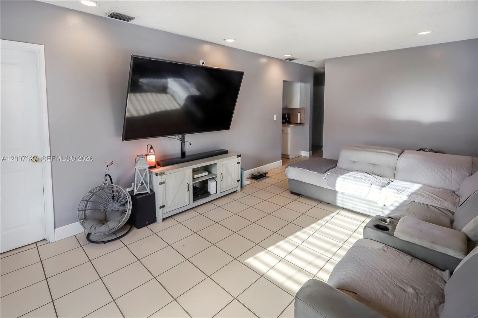 A living room features a large wall-mounted television, a media console, and a sectional sofa — 571 E 60th St, Hialeah FL 33013, HIALEAH, FL