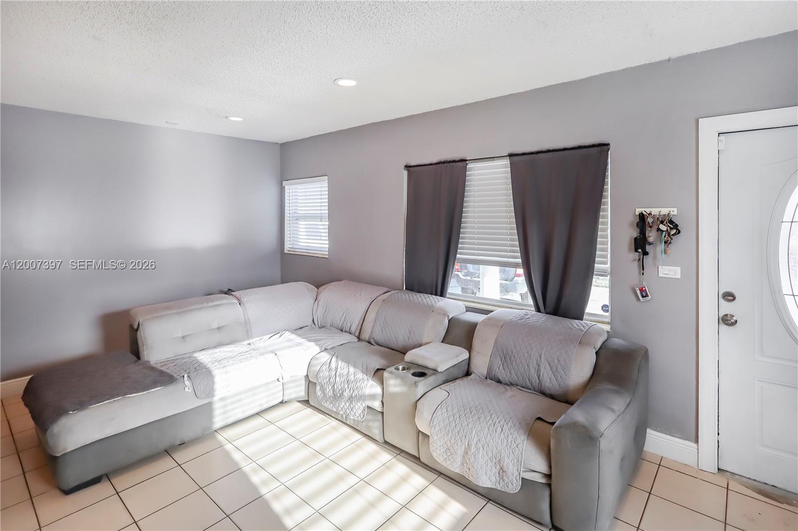 A living room features a large gray sectional sofa, tile flooring, and a white door — 571 E 60th St, Hialeah FL 33013, HIALEAH, FL