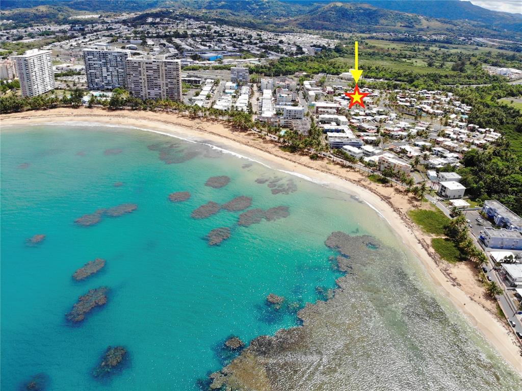 An aerial view shows a coastal neighborhood with a beach, coral reefs, and high-rise buildings — 144 PLAZA VIRGEN GORDA, LUQUILLO, PR