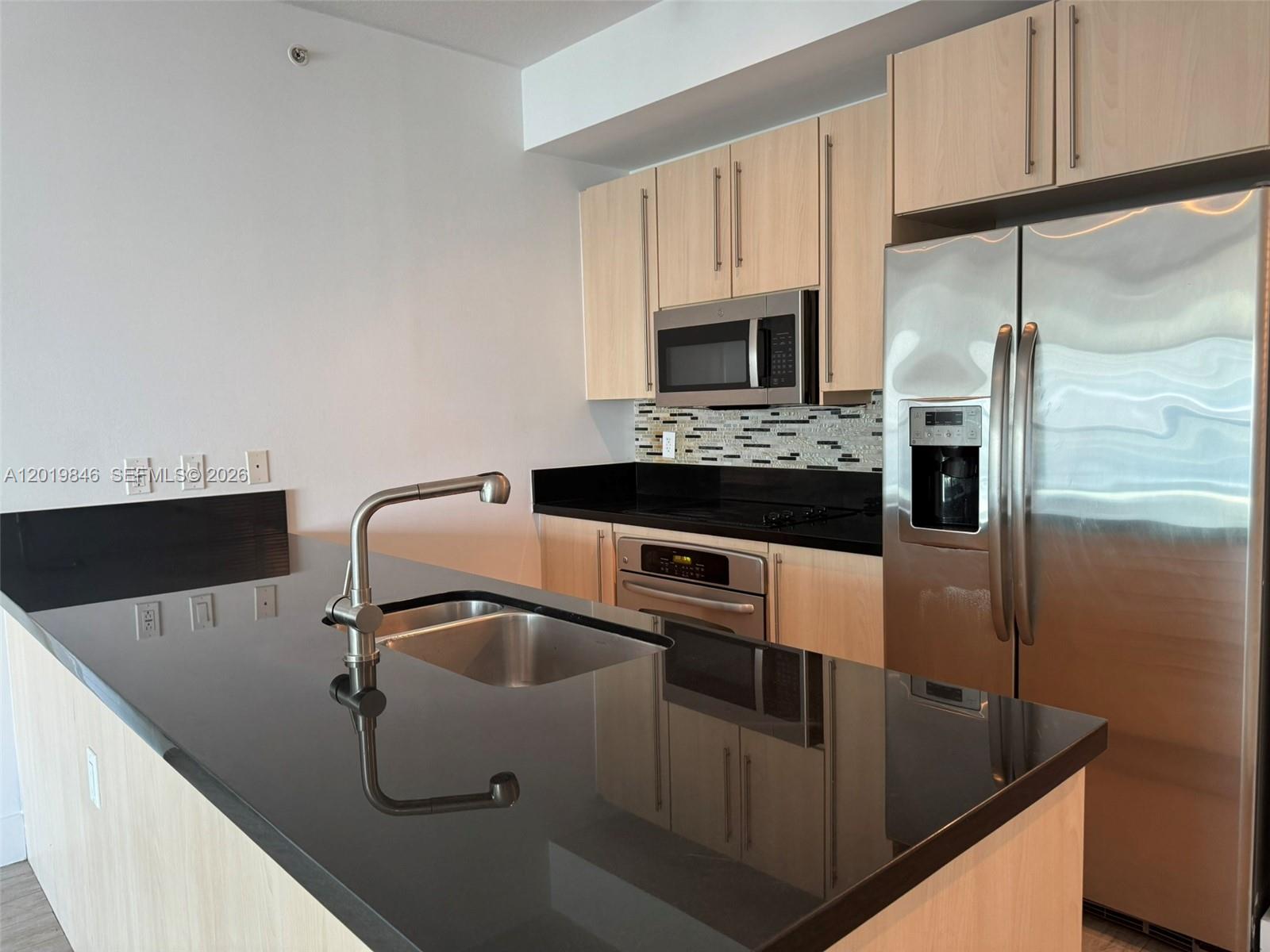A kitchen features light wood cabinets, black countertops, stainless steel appliances, and a central island — 79 SW 12th St, Miami FL 33130, MIAMI, FL