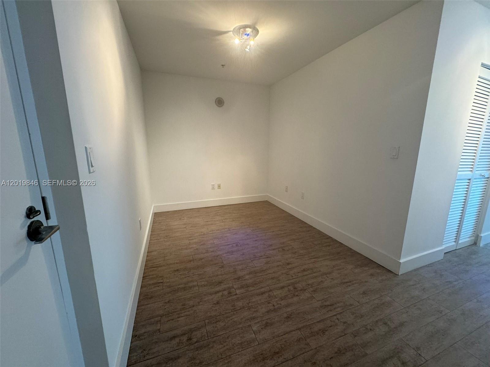 An empty room features white walls, wood-look tile flooring, and a modern ceiling light fixture — 79 SW 12th St, Miami FL 33130, MIAMI, FL