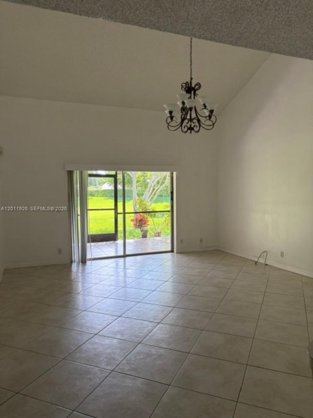 A living room with vaulted ceilings, tile flooring, a chandelier, and a sliding glass door — 667 Woodgate Ln # B, Sunrise FL 33326, SUNRISE, FL