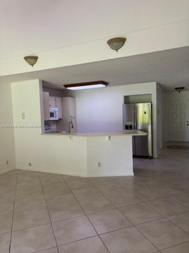 A kitchen with white cabinets and a breakfast bar opens into a tiled living area — 667 Woodgate Ln # B, Sunrise FL 33326, SUNRISE, FL