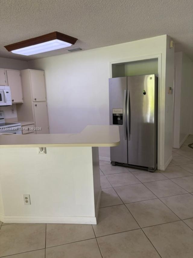 A kitchen features white cabinets, a stainless steel refrigerator, and a peninsula counter — 667 Woodgate Ln # B, Sunrise FL 33326, SUNRISE, FL