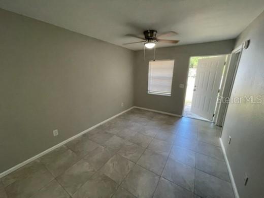 An empty room with gray walls, tiled floors, a ceiling fan, and an open exterior door — 12136 MUNBURY DRIVE UNIT 2, DADE CITY, FL