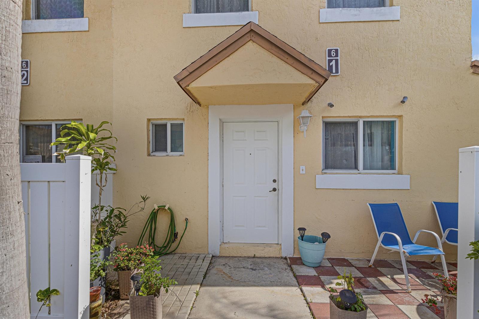 The exterior of a yellow townhouse features a white front door and a small patio — 6631 Winfield Boulevard # 6, Margate FL 33063, MARGATE, FL