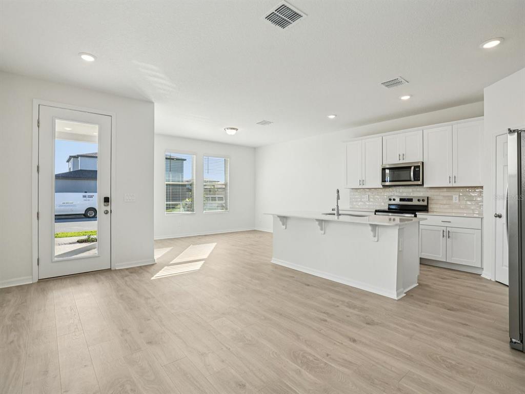 A bright kitchen features white cabinets, a central island, and light wood-look flooring — 4689 CROSS PRAIRIE PARKWAY, ST CLOUD, FL