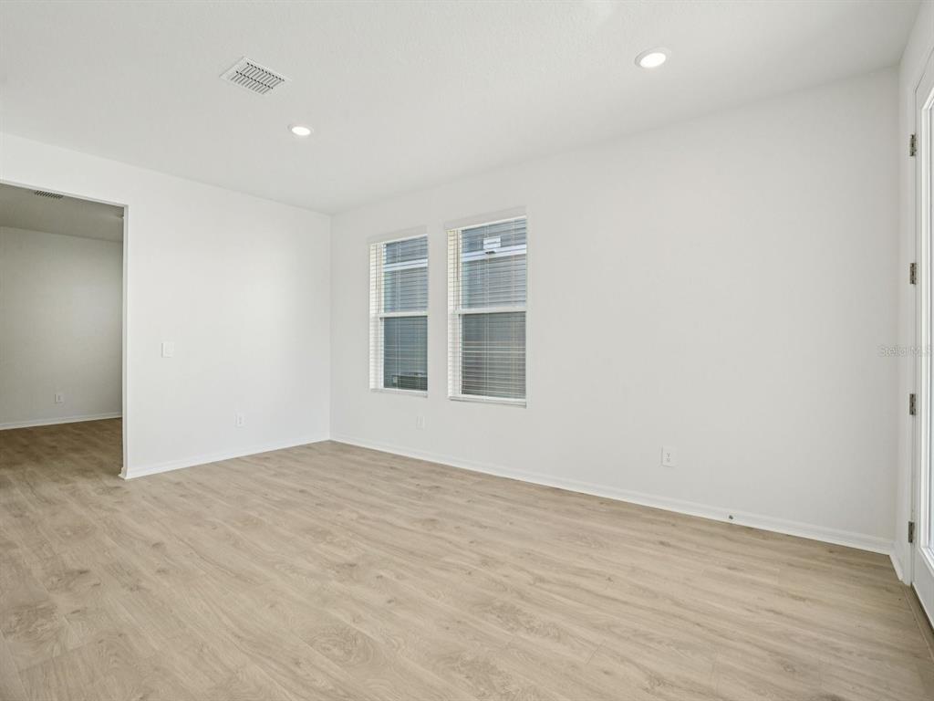 An empty room features light wood-look flooring, white walls, two windows, and recessed lighting — 4689 CROSS PRAIRIE PARKWAY, ST CLOUD, FL
