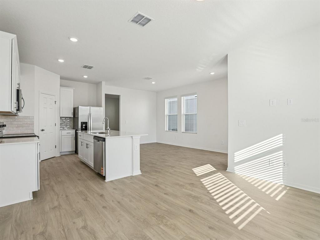 A bright, open-concept kitchen and living area features white cabinetry, stainless steel appliances, and wood-look flooring — 4689 CROSS PRAIRIE PARKWAY, ST CLOUD, FL