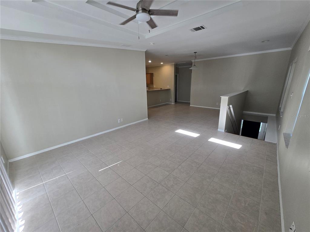 An open-concept living area features light-colored tile flooring, a ceiling fan, and a staircase — 7644 SAILWINDS PASS, PORT RICHEY, FL