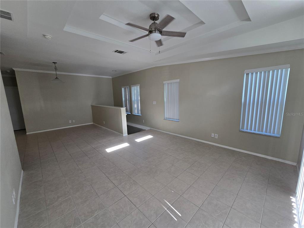 An empty living room features tile flooring, a tray ceiling with a fan, and windows — 7644 SAILWINDS PASS, PORT RICHEY, FL