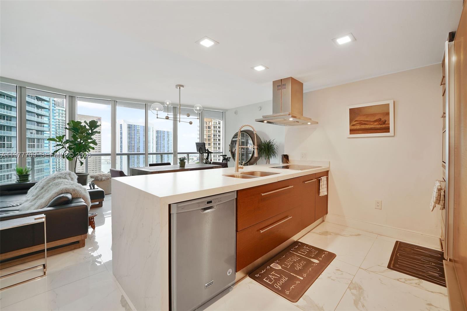 A modern kitchen features a waterfall island, wood cabinetry, and floor-to-ceiling windows with city views — 495 Brickell Ave # 2804, Miami FL 33131, MIAMI, FL
