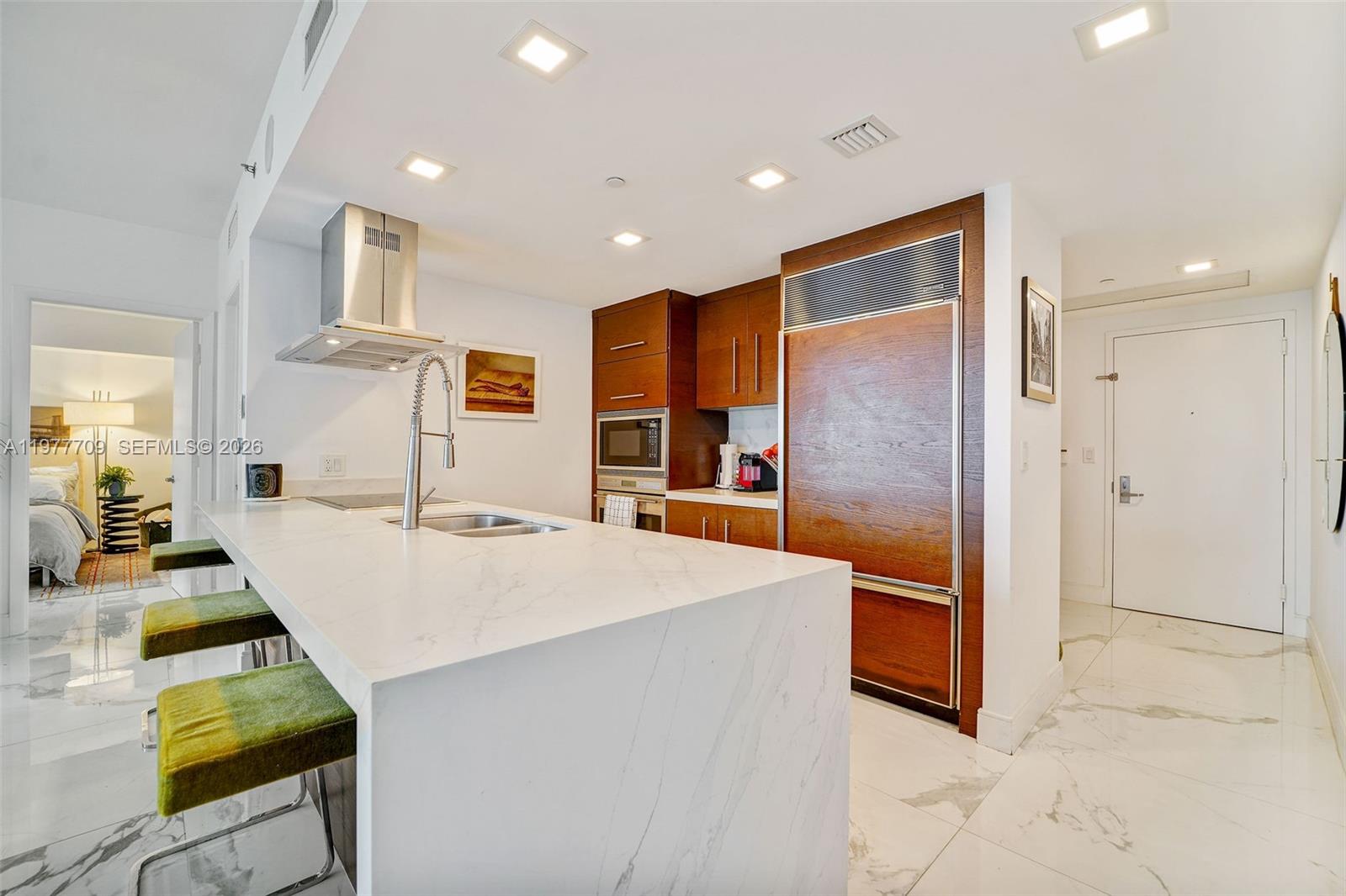 A modern kitchen features a marble waterfall island, wood cabinetry, and green bar stools — 495 Brickell Ave # 2804, Miami FL 33131, MIAMI, FL