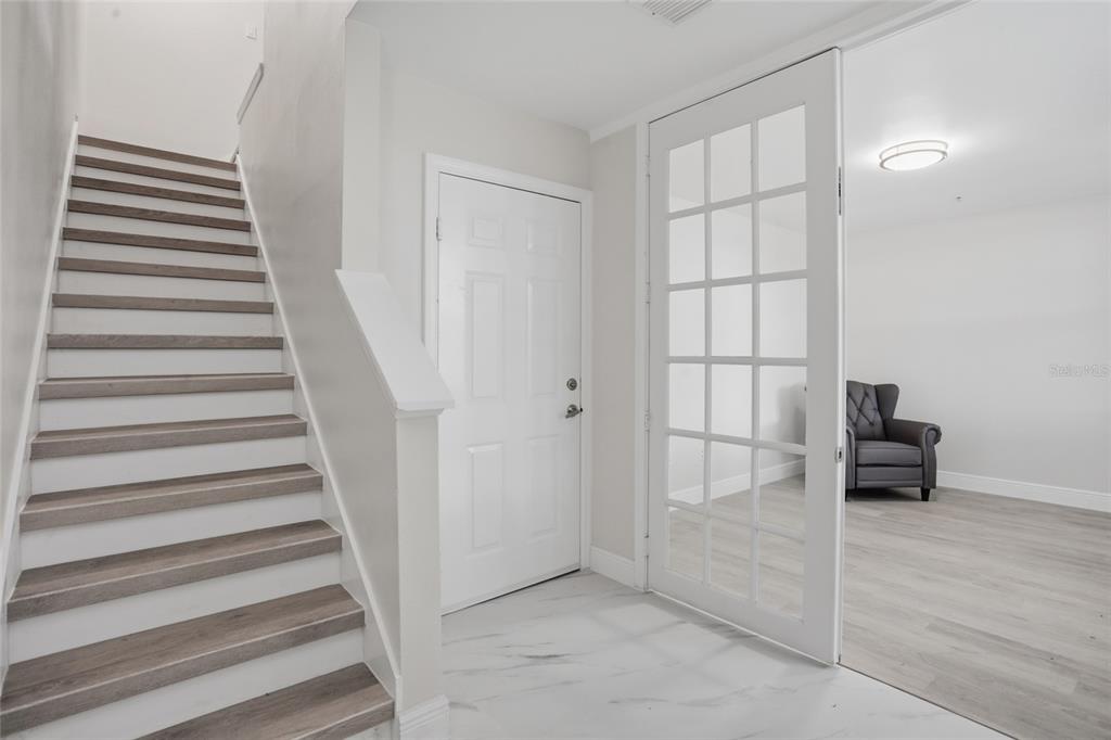 A foyer features a staircase with wood-look treads, a white door, and glass-paned double doors — 1056 WATERSIDE DRIVE, CELEBRATION, FL