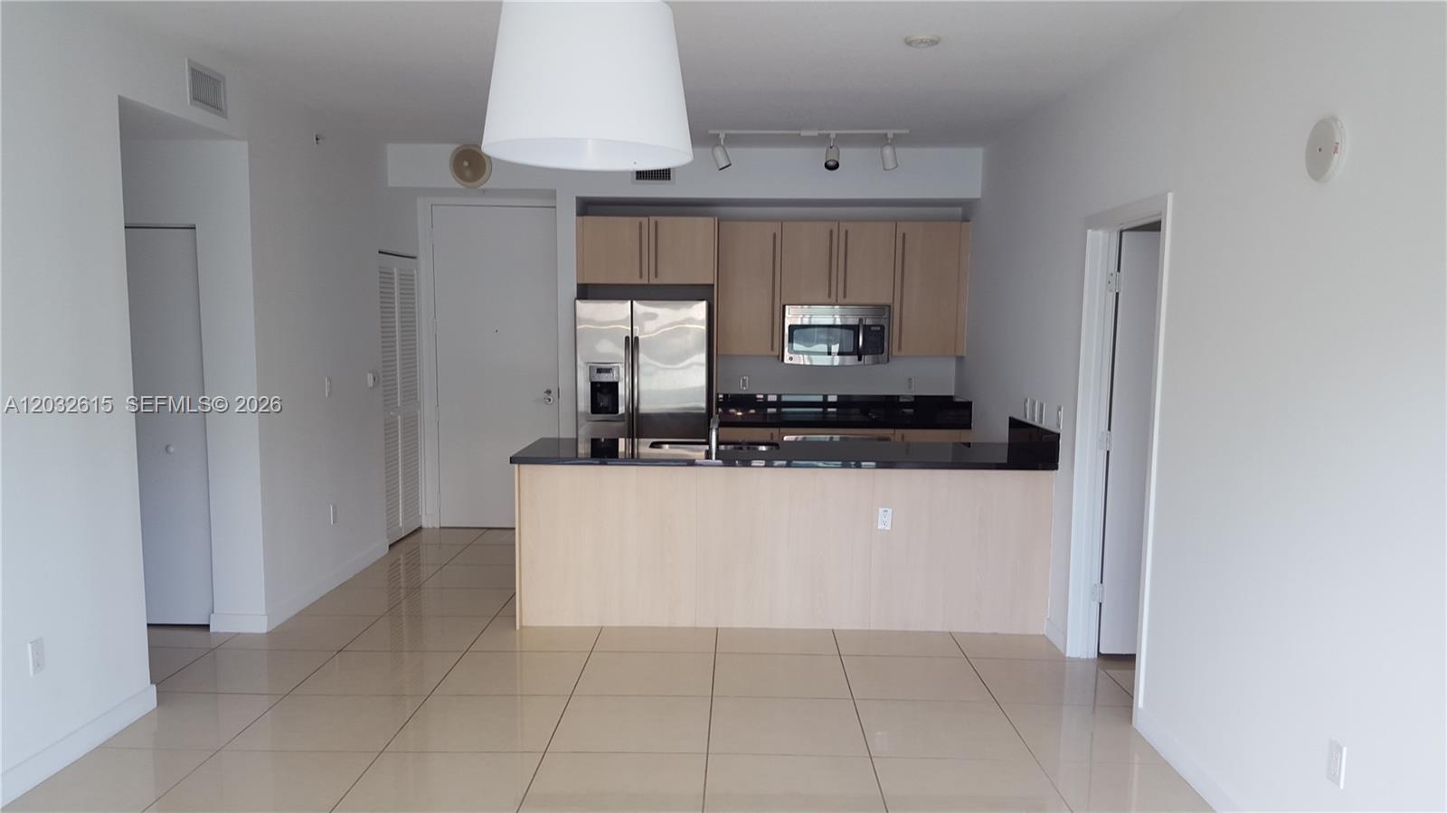 A kitchen with light wood cabinets, black countertops, and stainless steel appliances overlooks a room — 1111 SW 1  AVE, Miami FL 33130, MIAMI, FL