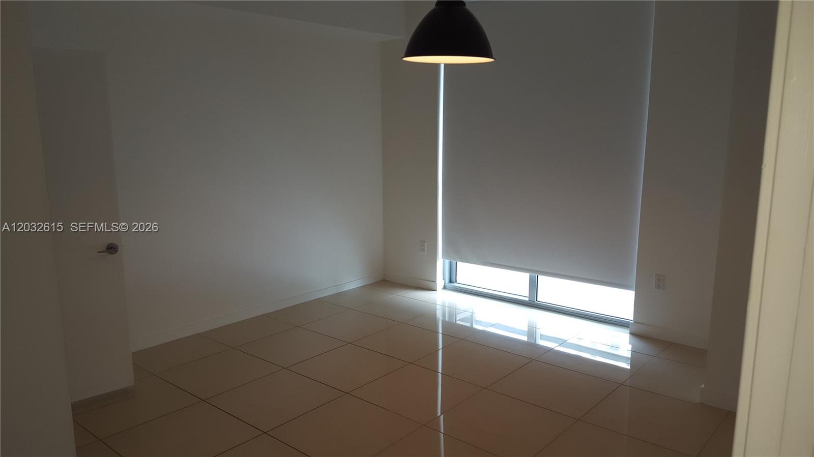 An empty room features light-colored tile flooring, a single pendant light, and a large window — 1111 SW 1  AVE, Miami FL 33130, MIAMI, FL