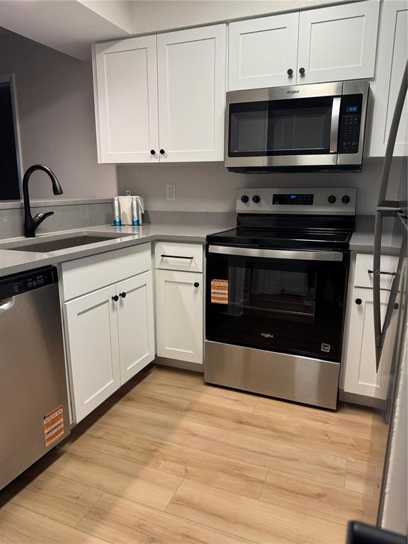 A kitchen features white cabinets, stainless steel appliances, a black faucet, and wood-look flooring — 4786 FOX HUNT DRIVE UNIT D743, WESLEY CHAPEL, FL