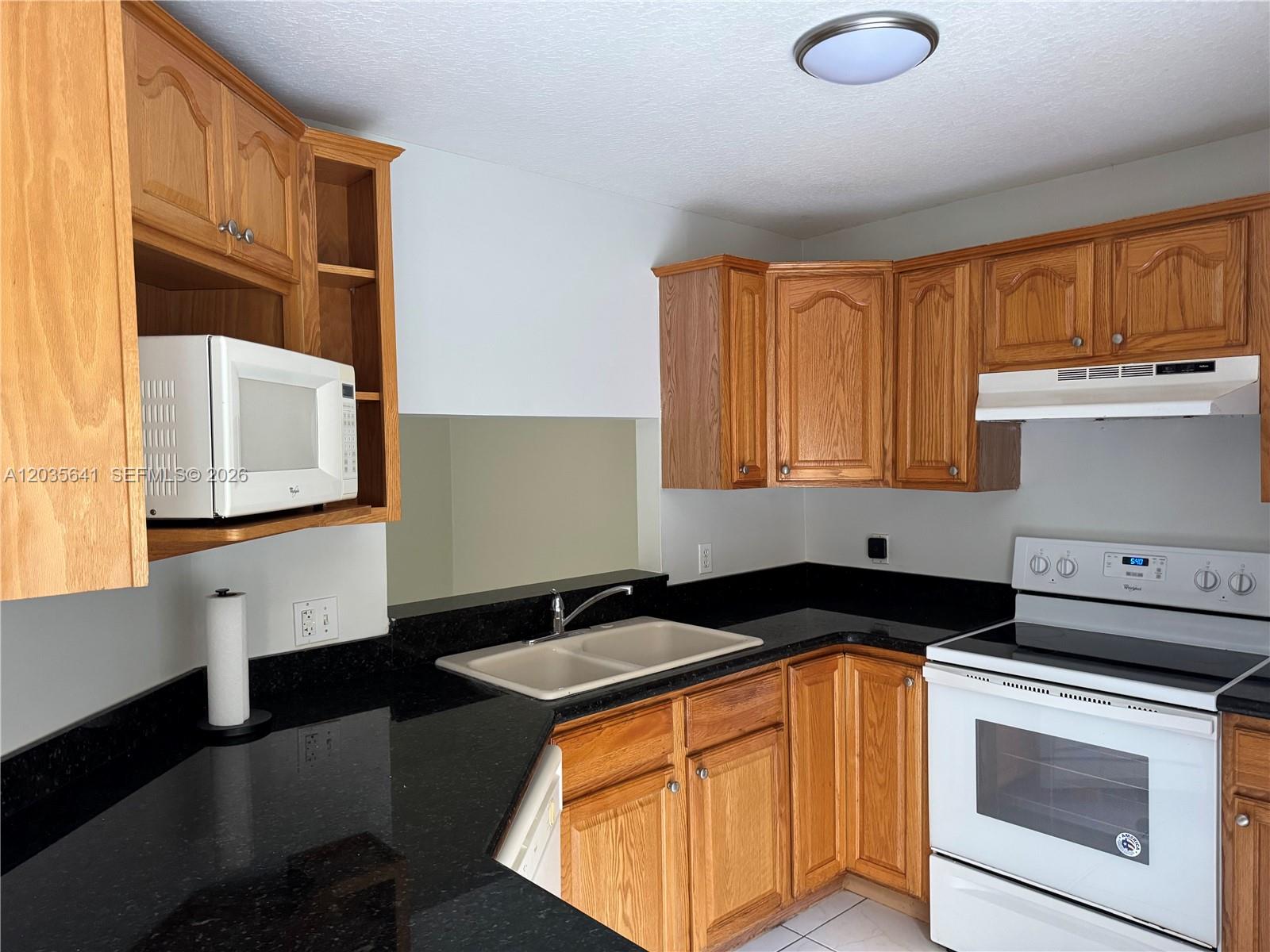 A kitchen features oak cabinets, black countertops, a white stove, and a double sink — 3811 Simms St # 0, Hollywood FL 33021, HOLLYWOOD, FL