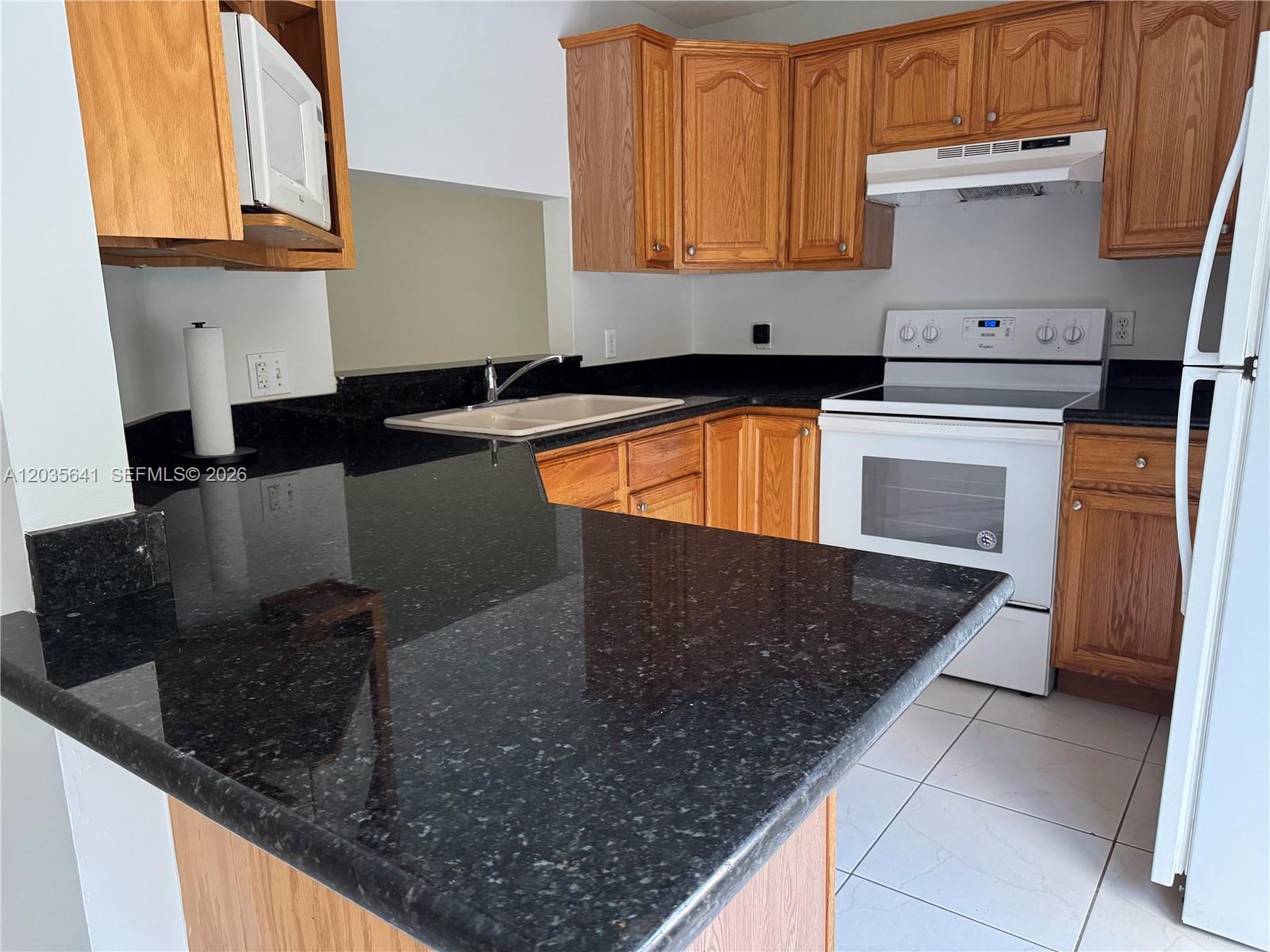 A kitchen features oak cabinets, black granite countertops, white appliances, and light-colored floor tiles — 3811 Simms St # 0, Hollywood FL 33021, HOLLYWOOD, FL