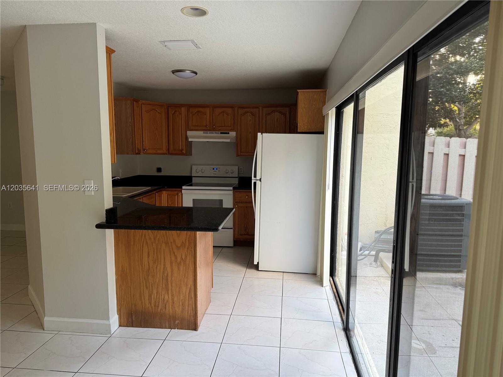 A kitchen features wood cabinets, black countertops, white appliances, and a sliding glass door — 3811 Simms St # 0, Hollywood FL 33021, HOLLYWOOD, FL