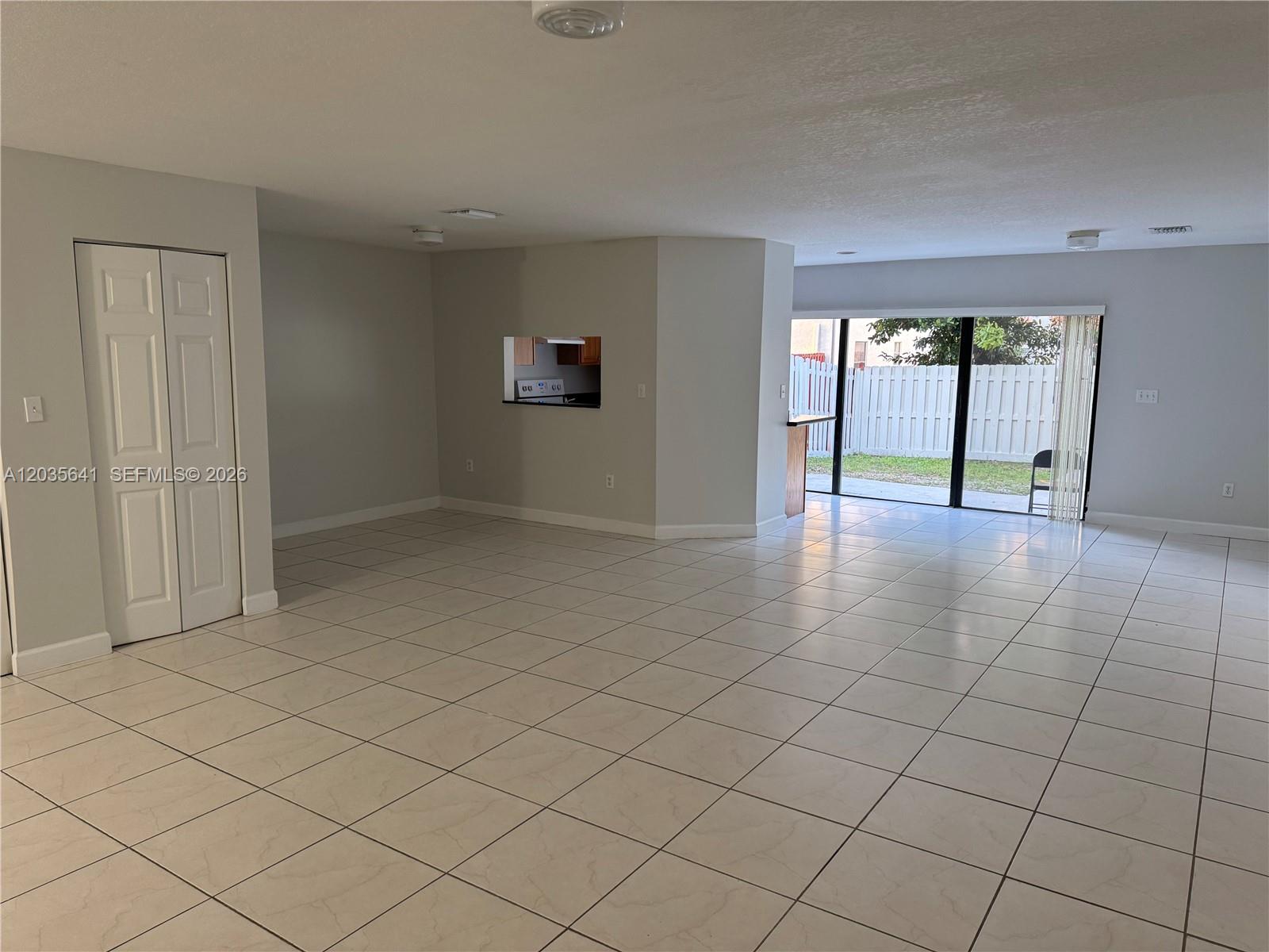 An open-concept living area features light-colored tile floors, a kitchen pass-through window, and sliding glass doors — 3811 Simms St # 0, Hollywood FL 33021, HOLLYWOOD, FL