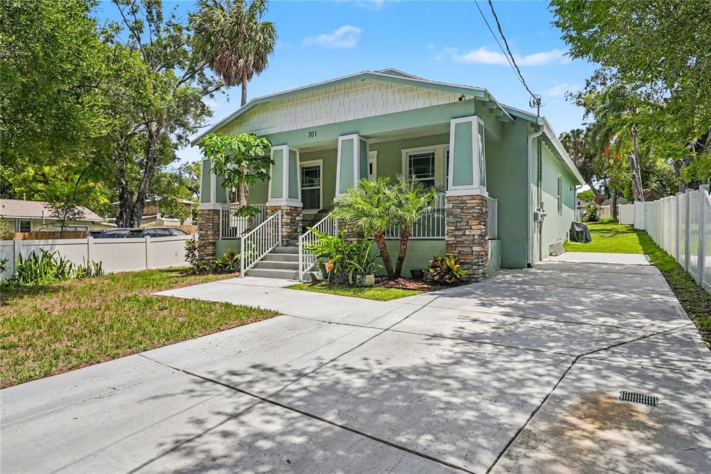 A green bungalow with a stone-accented porch and a concrete driveway under a blue sky — 701 E HOLLYWOOD STREET, TAMPA, FL