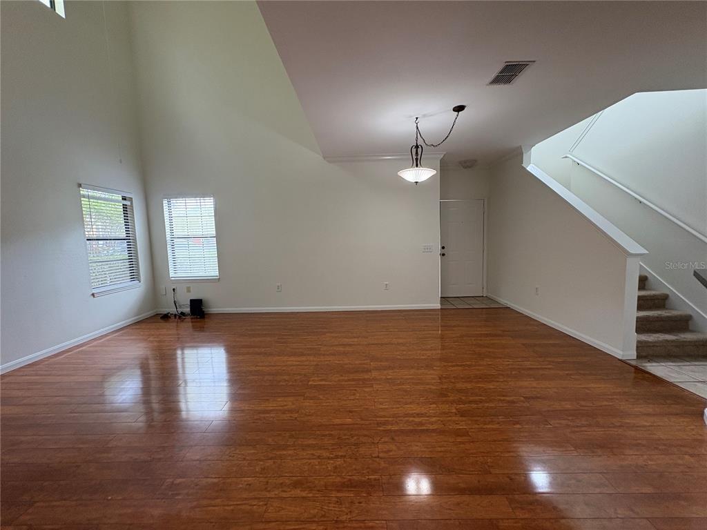 An empty living room features high ceilings, hardwood floors, a staircase, and a hanging light fixture — 2277 CHIANTI PLACE UNIT 37, PALM HARBOR, FL