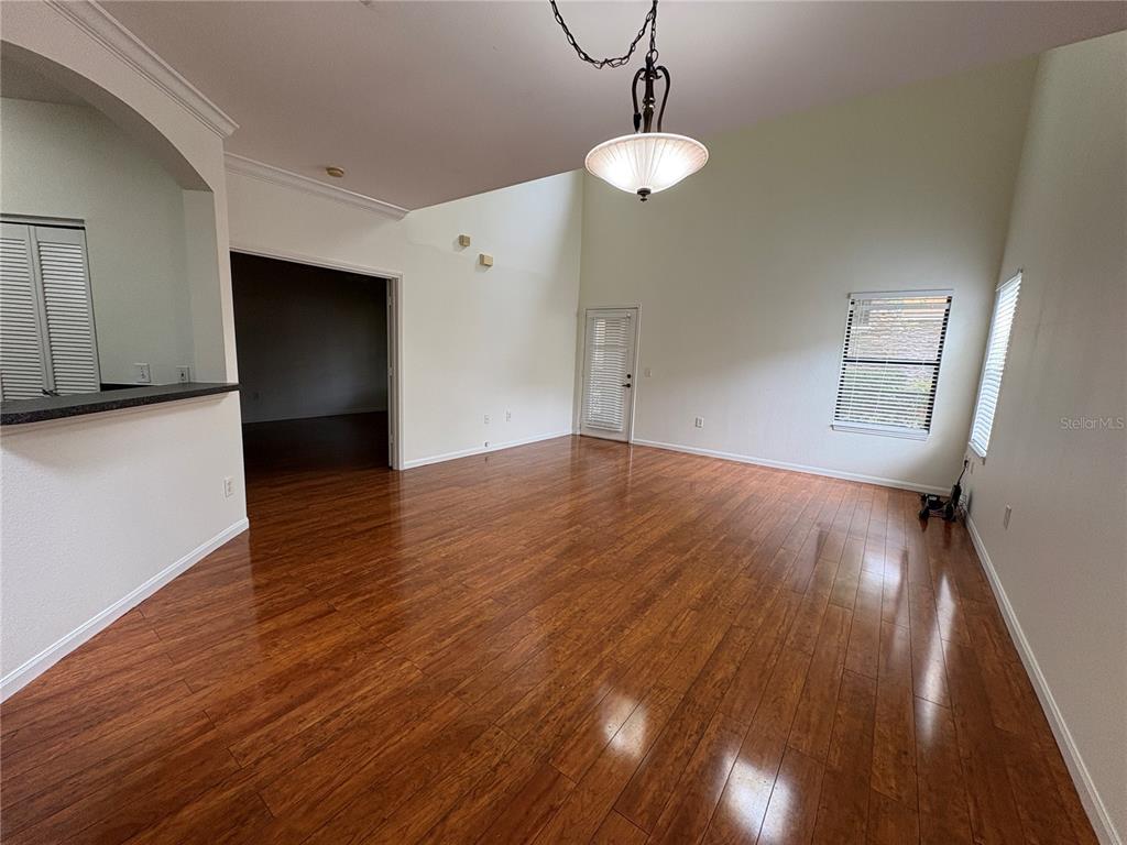 An empty living room features high ceilings, hardwood flooring, a pendant light, and two windows — 2277 CHIANTI PLACE UNIT 37, PALM HARBOR, FL