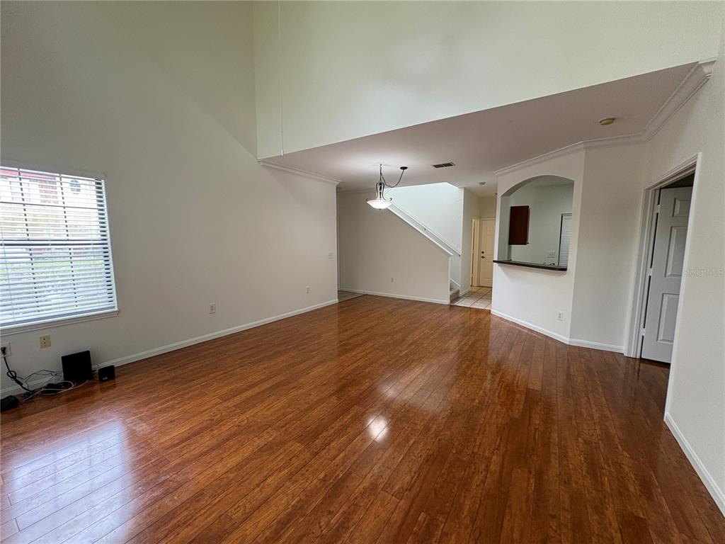 An empty living room with high ceilings, hardwood floors, and a staircase in the background — 2277 CHIANTI PLACE UNIT 37, PALM HARBOR, FL