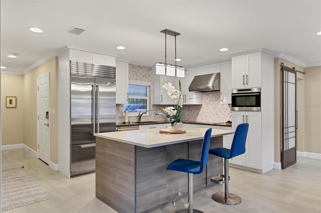 A modern kitchen features a gray island with blue bar stools and white cabinetry — 1900 BENJAMIN FRANKLIN DRIVE UNIT V-15, SARASOTA, FL