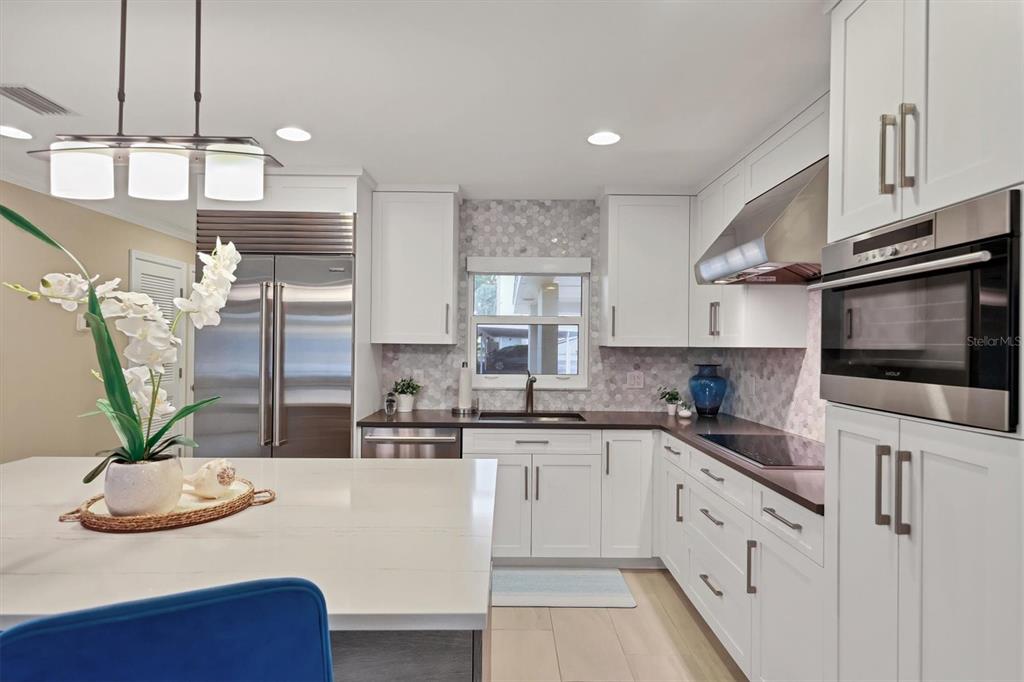 A modern kitchen features white cabinetry, stainless steel appliances, a quartz island, and hexagonal backsplash tile — 1900 BENJAMIN FRANKLIN DRIVE UNIT V-15, SARASOTA, FL