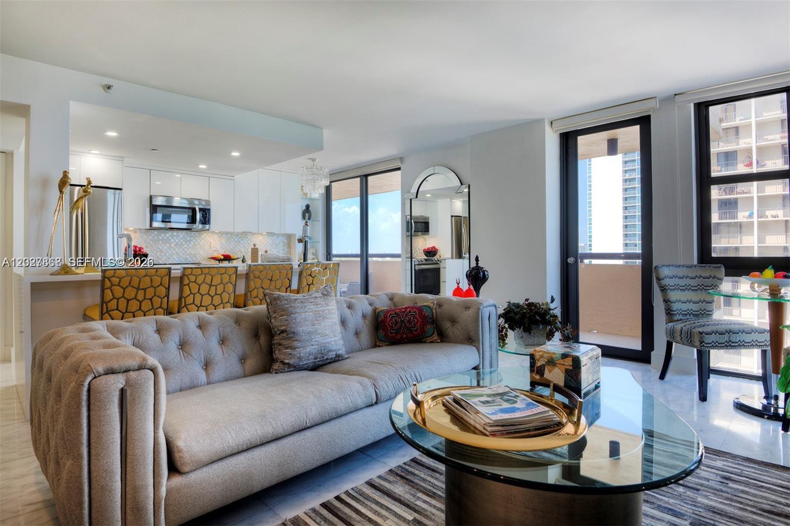 A modern living room features a tufted gray sofa, glass coffee table, and open kitchen — 2555 Collins Ave # 1400, Miami Beach FL 33140, MIAMI BEACH, FL