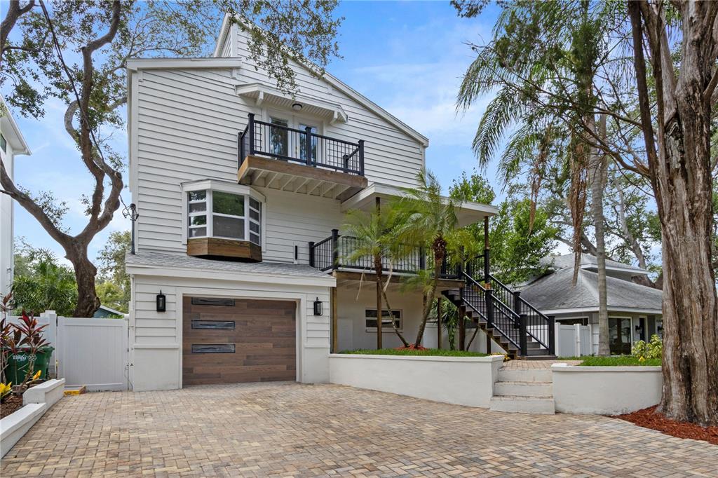 A three-story house with white siding, a wood-paneled garage door, and an elevated wooden deck — 3232 W OAKELLAR AVENUE, TAMPA, FL