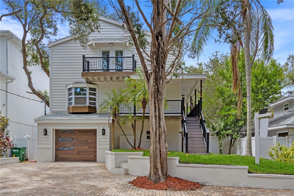 A three-story house with a wooden garage door, a front balcony, and a paved driveway — 3232 W OAKELLAR AVENUE, TAMPA, FL
