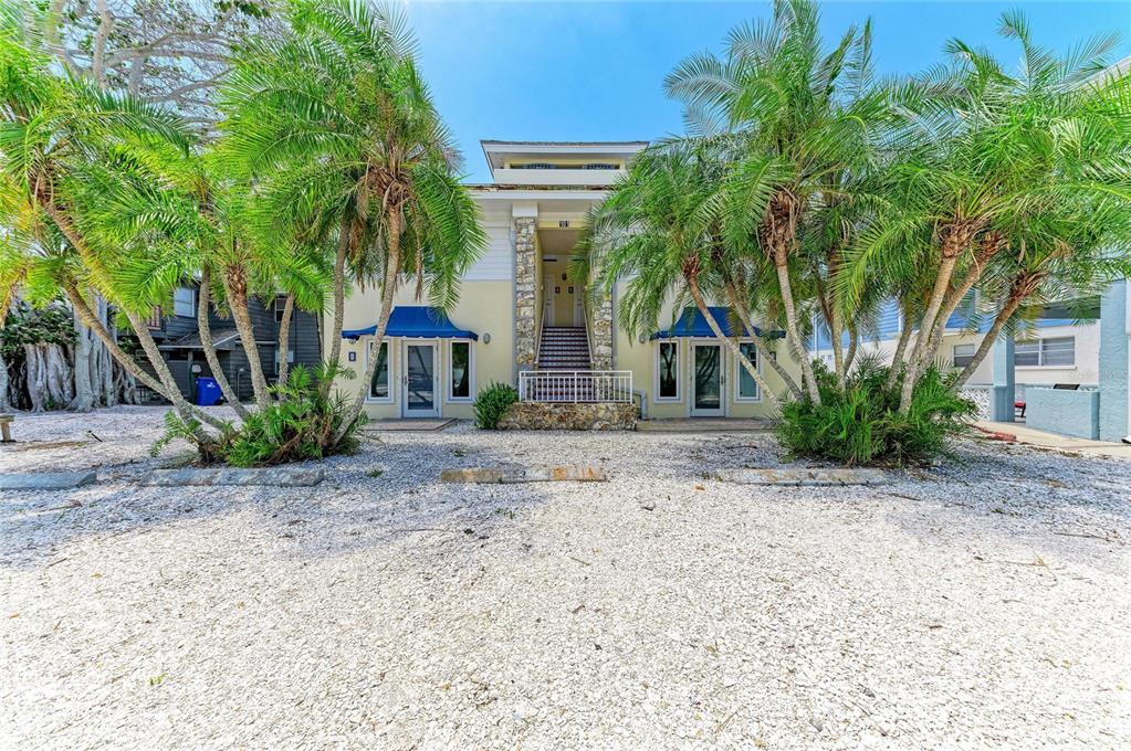A two-story building with palm trees, blue awnings, and a gravel parking area in front — 101 PALM AVENUE UNIT 2, ANNA MARIA, FL