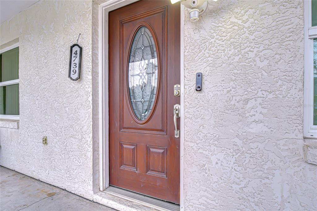 A wooden front door with an oval glass insert is set in a textured stucco wall — 4739 SILVER CIRCLE, ZEPHYRHILLS, FL