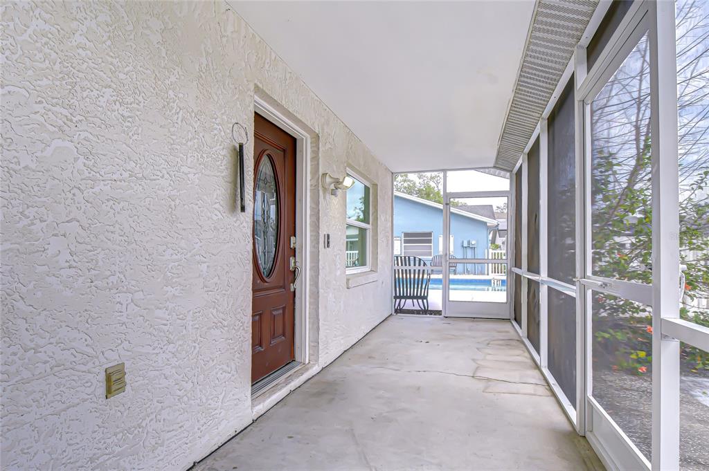 A covered, screened-in porch features a brown front door and a view of a pool — 4739 SILVER CIRCLE, ZEPHYRHILLS, FL