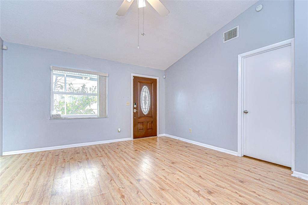 An empty room features light blue walls, wood-look flooring, a ceiling fan, and a front door — 4739 SILVER CIRCLE, ZEPHYRHILLS, FL