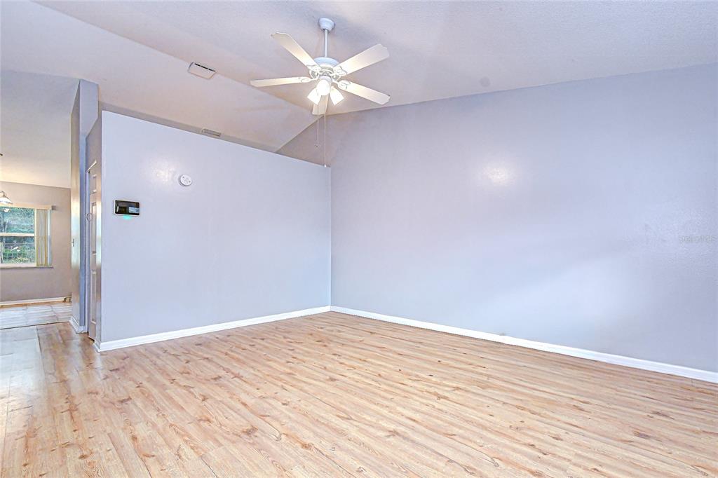 A living room with light gray walls, wood-look flooring, and a vaulted ceiling with a fan — 4739 SILVER CIRCLE, ZEPHYRHILLS, FL