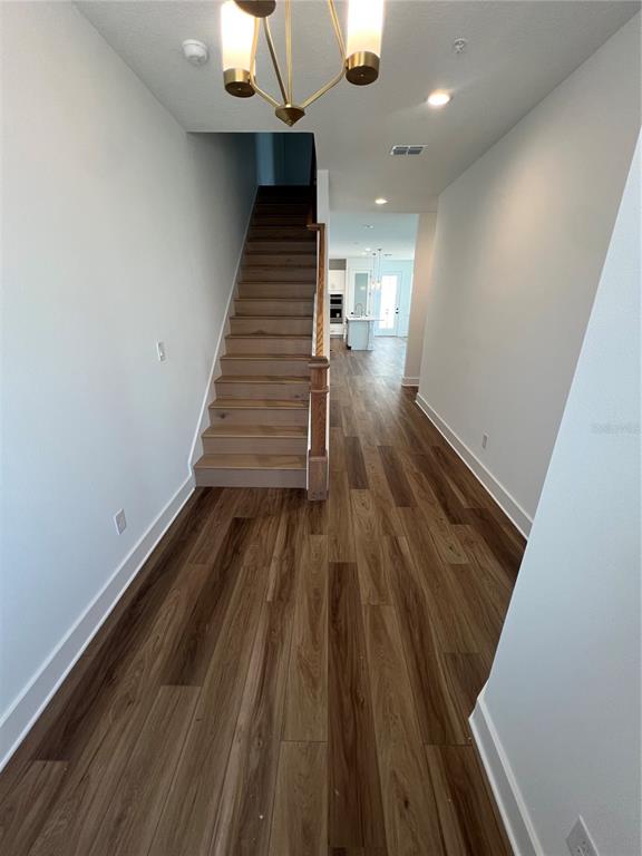 A hallway with wood-look flooring leads to a staircase and a kitchen in the distance — 1876 CROWNCREST DRIVE, APOPKA, FL