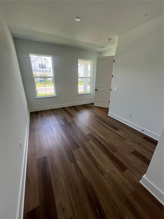 An empty room with wood-look flooring, two windows, and a white interior door — 1876 CROWNCREST DRIVE, APOPKA, FL