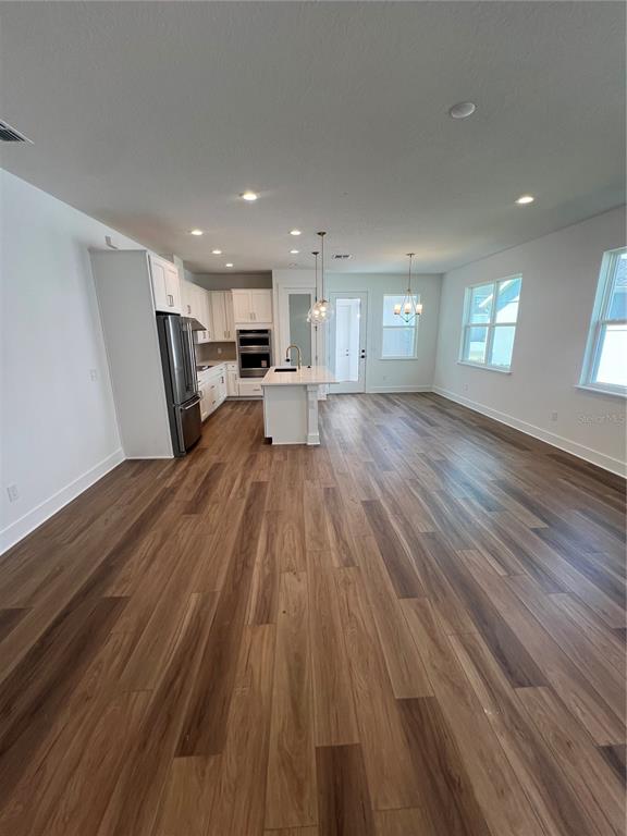 A bright, open-concept kitchen and living area featuring wood-look flooring and white cabinetry — 1876 CROWNCREST DRIVE, APOPKA, FL