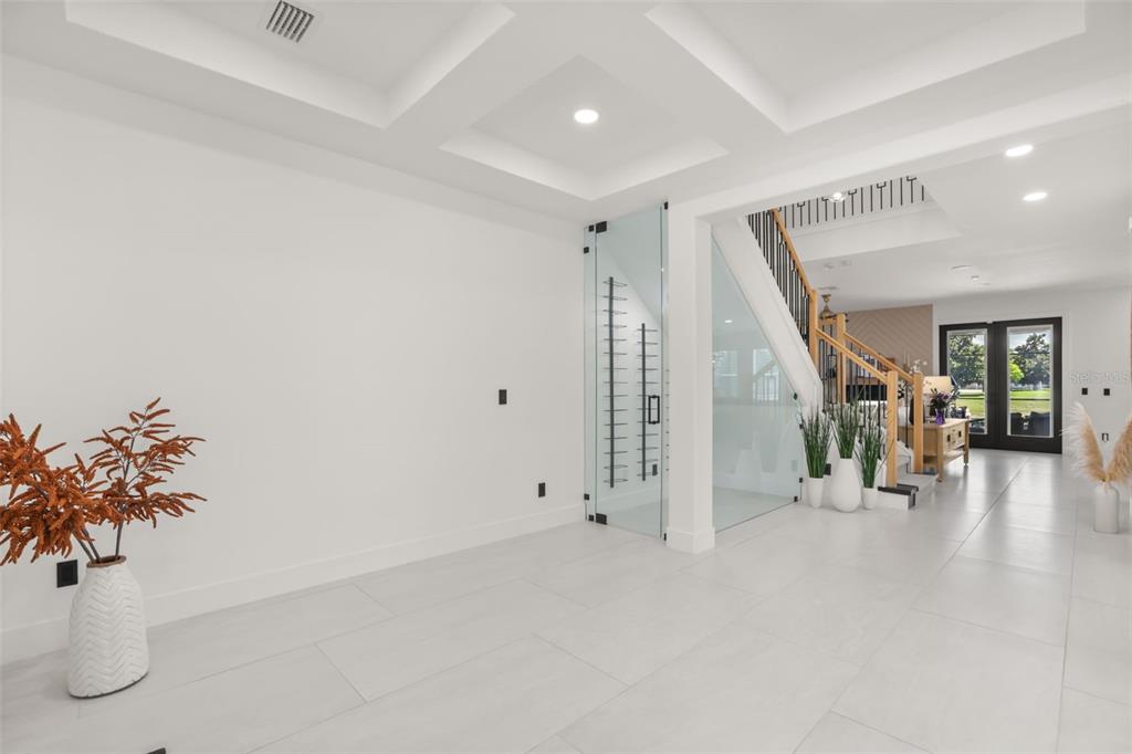 A bright, modern foyer features white tile floors, a glass-enclosed wine cellar, and a staircase — 11716 SHELTERING PINE DRIVE, ORLANDO, FL