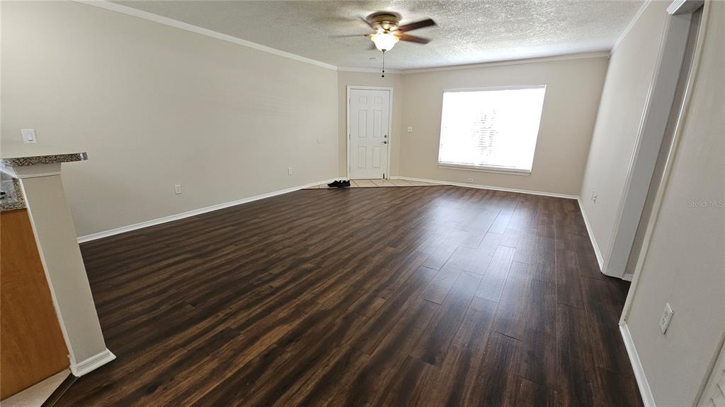 An empty living room features dark wood-look flooring, beige walls, and a ceiling fan — 3651 N GOLDENROD ROAD UNIT A103, WINTER PARK, FL