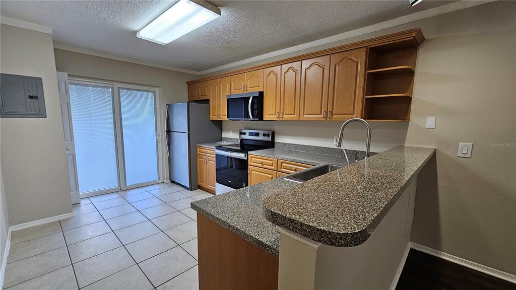 A kitchen features wood cabinets, granite countertops, stainless steel appliances, and tile flooring — 3651 N GOLDENROD ROAD UNIT A103, WINTER PARK, FL