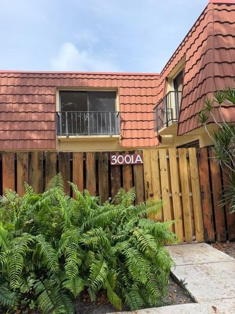 A two-story building exterior features a brown tile roof, a balcony, and a wooden fence — 3001 San Clara Drive # a, Delray Beach FL 33445, DELRAY BEACH, FL